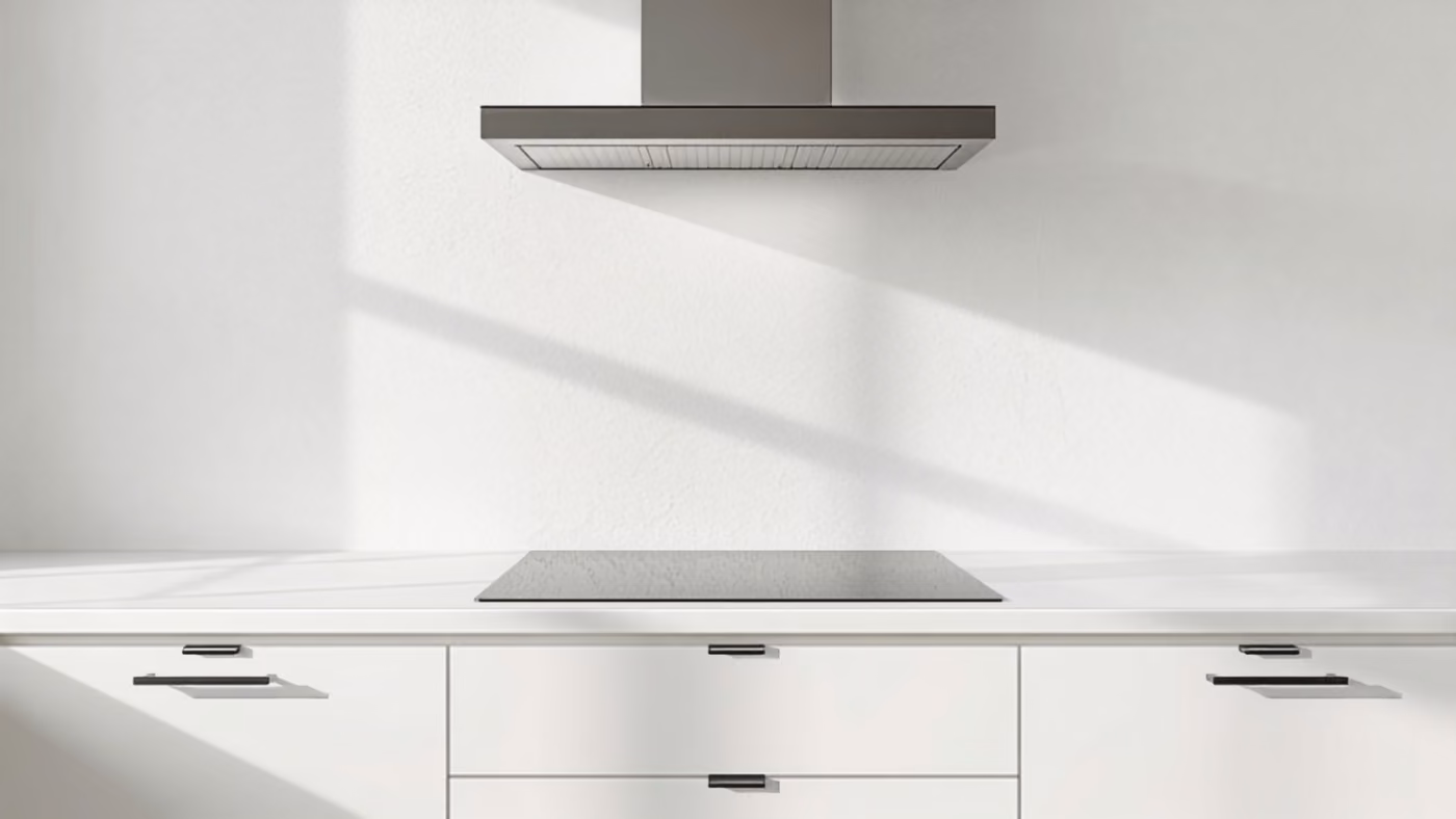 A stainless chimney range hood mounted on a white plaster wall above a black glass cooktop set in a white counter with drawers below